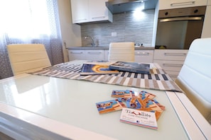 A modern kitchen with white cabinets, stainless steel appliances, and a striped rug on the table.