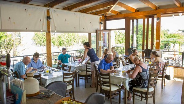 Un espace de restauration en plein air avec des tables et des chaises en bois, de grandes fenêtres et une vue sur la verdure.