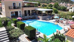 A hotel with a swimming pool, outdoor seating, and a view of the surrounding hills.
