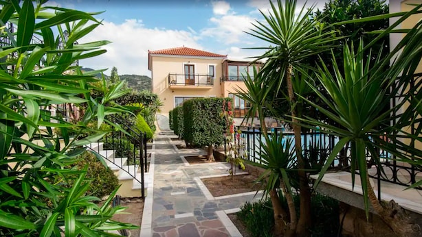 A pathway leading to a building with a tiled roof and a pool on the right.
