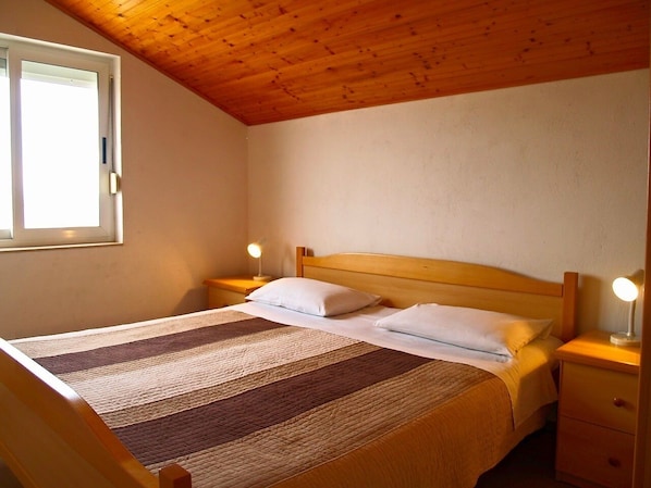 A single bed with a wooden headboard, two bedside tables with lamps, and a window with blinds.