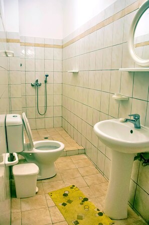 Efficient bathroom with toilet, bidet, and sink, featuring a tiled floor and convenient mirror.