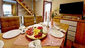 Un comedor con una mesa de madera dispuesta para cuatro personas, una escalera y un televisor de pantalla plana montado en la pared.