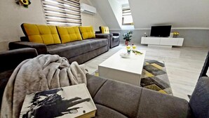 Una sala de estar moderna con un sofá gris, cojines amarillos, una mesa de centro blanca y una estantería.