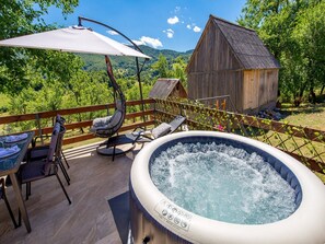 A hot tub on a wooden deck with a hanging chair and a table, surrounded by a wooden fence and a wooden building. - Matan House (Otocac)