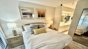 Une chambre d’hôtel avec un grand lit, deux tables de chevet avec des lampes, un miroir et des œuvres d’art accrochées aux murs.