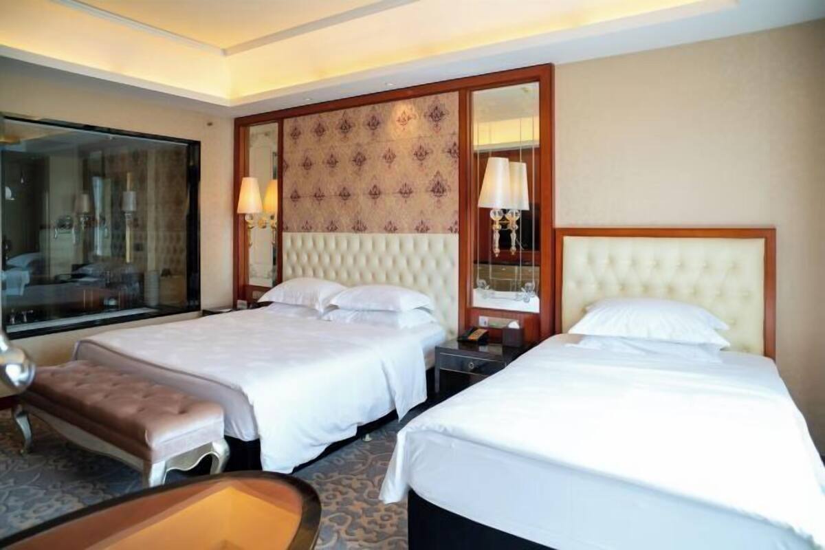 A hotel room with two beds, a large mirror, and a small table.