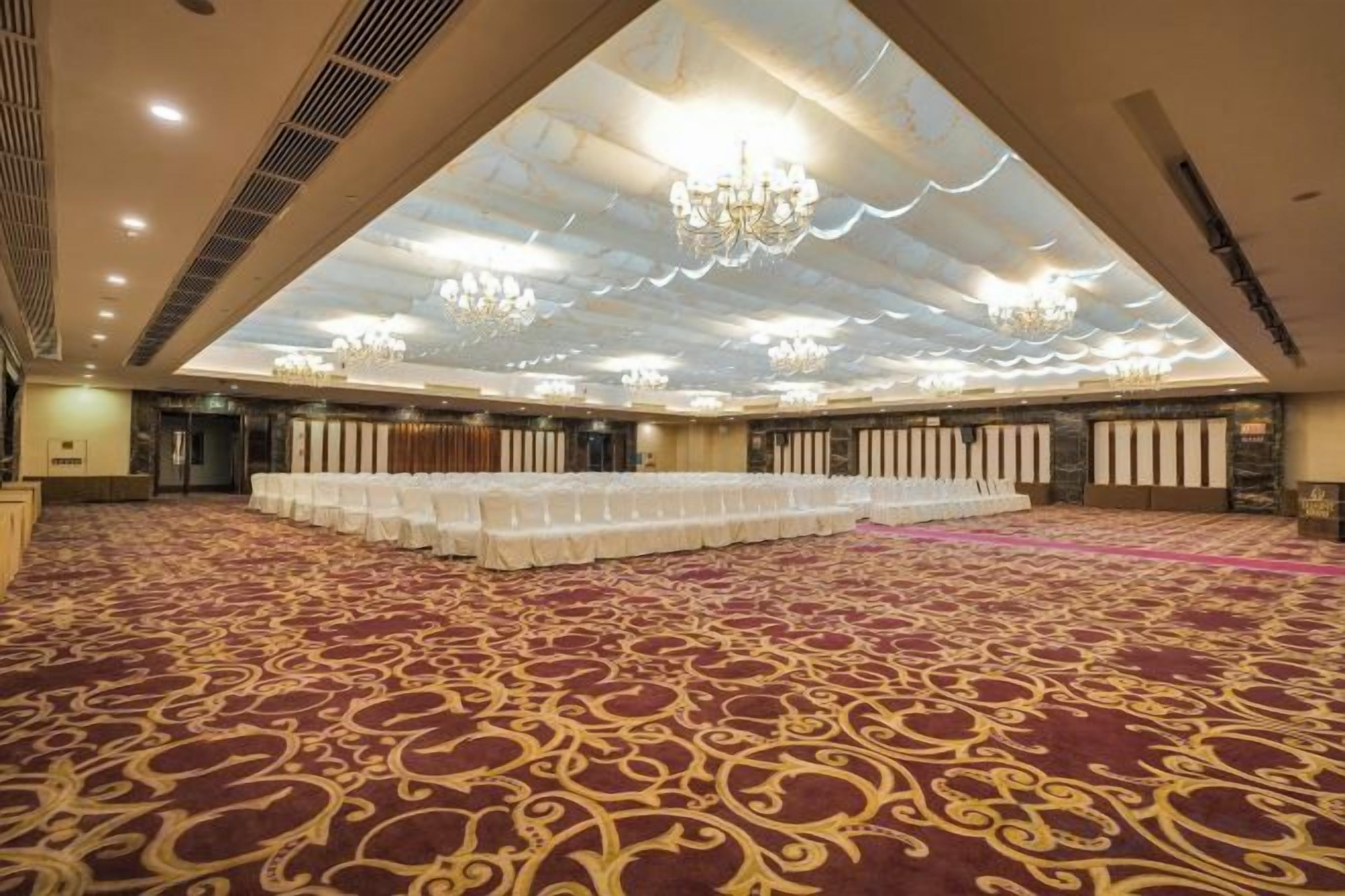 A large hall with rows of tables, a patterned carpet, and a high ceiling with chandeliers.