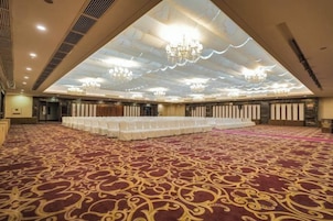 Un salón amplio con filas de mesas, una alfombra estampada y un techo alto con candelabros.