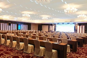 Un salón de conferencias con mesas y sillas dispuestas en filas, una pantalla grande y candelabros.