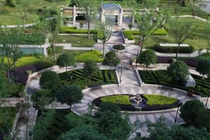 An aerial view of a landscaped area with a central circular garden, pathways, and a building with a dome-shaped roof. - Jasmine International Hotel (Renshou)