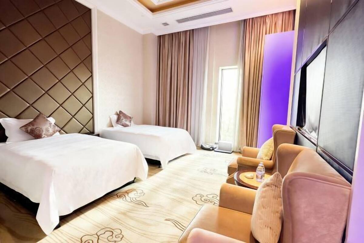 A hotel room with two beds, a sofa, a TV, and a large window with curtains.