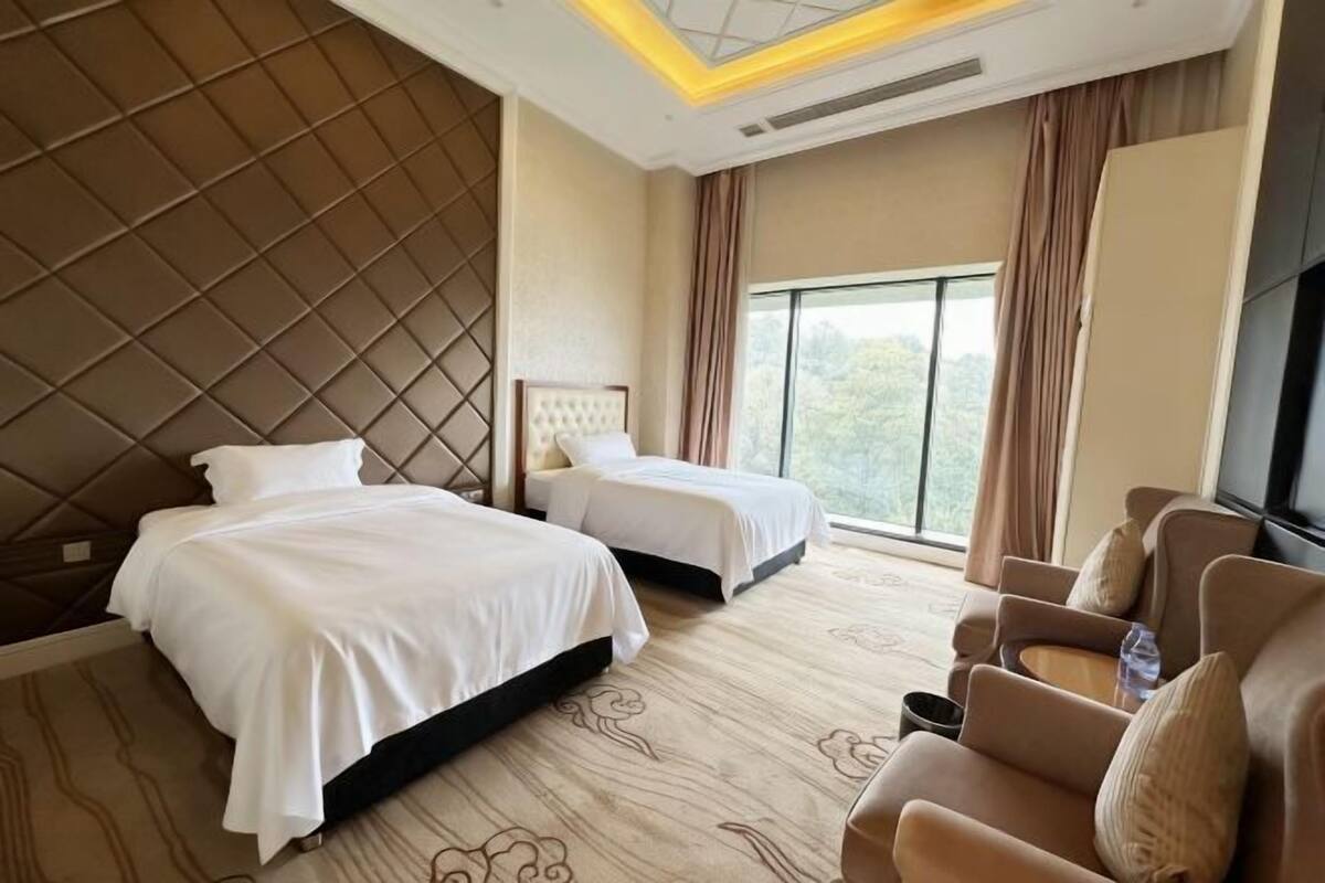 A hotel room with two beds, a sofa, a TV, and a large window.