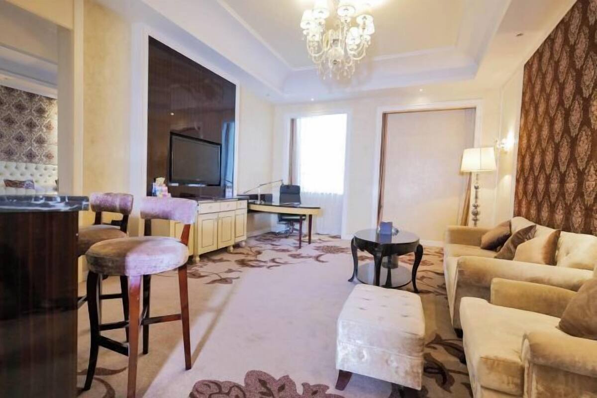 A living room with a sofa, ottoman, and bar stools. There is a television and a small table with a lamp.