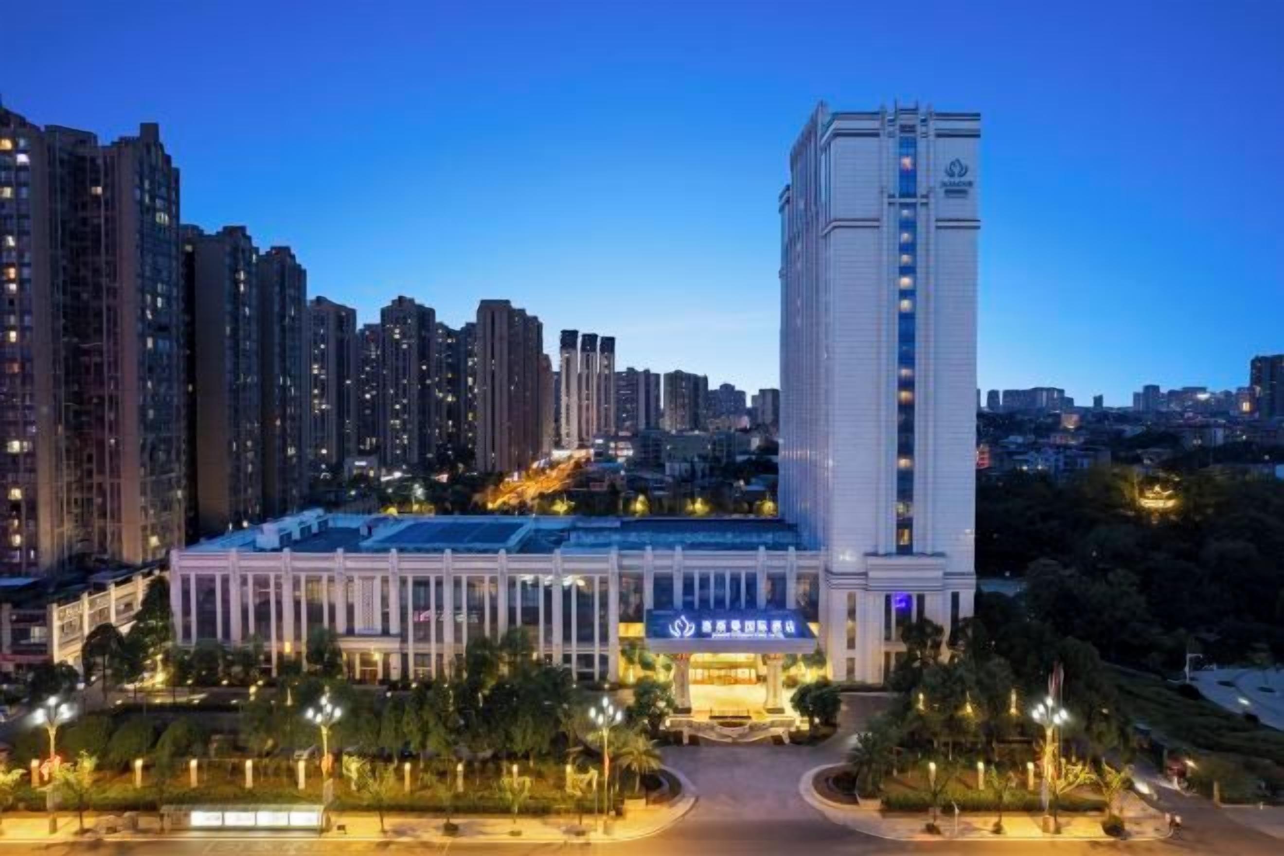 Un hotel moderno con patio central, rodeado de edificios altos, bajo un cielo despejado al atardecer.