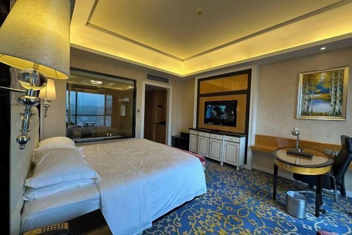 A hotel room with a large bed, a TV, a small table, and a painting on the wall.
