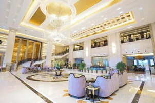 A spacious lobby with a grand chandelier, a central seating area, and a staircase leading to upper floors.