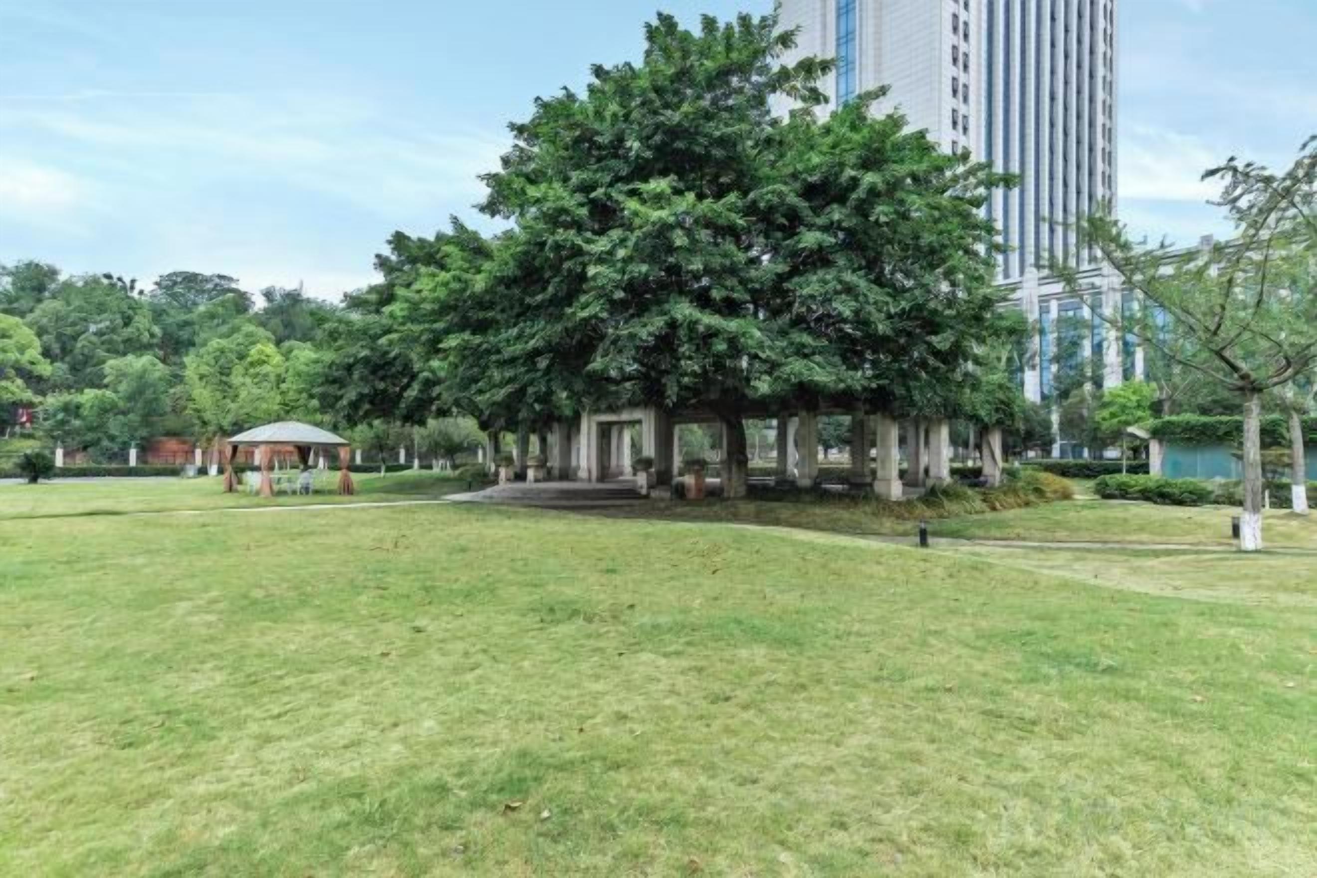 A park with a gazebo, a grassy area, and a tall building in the background.