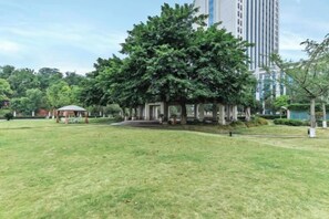 A park with a gazebo, a grassy area, and a tall building in the background. - Jasmine International Hotel (Renshou)
