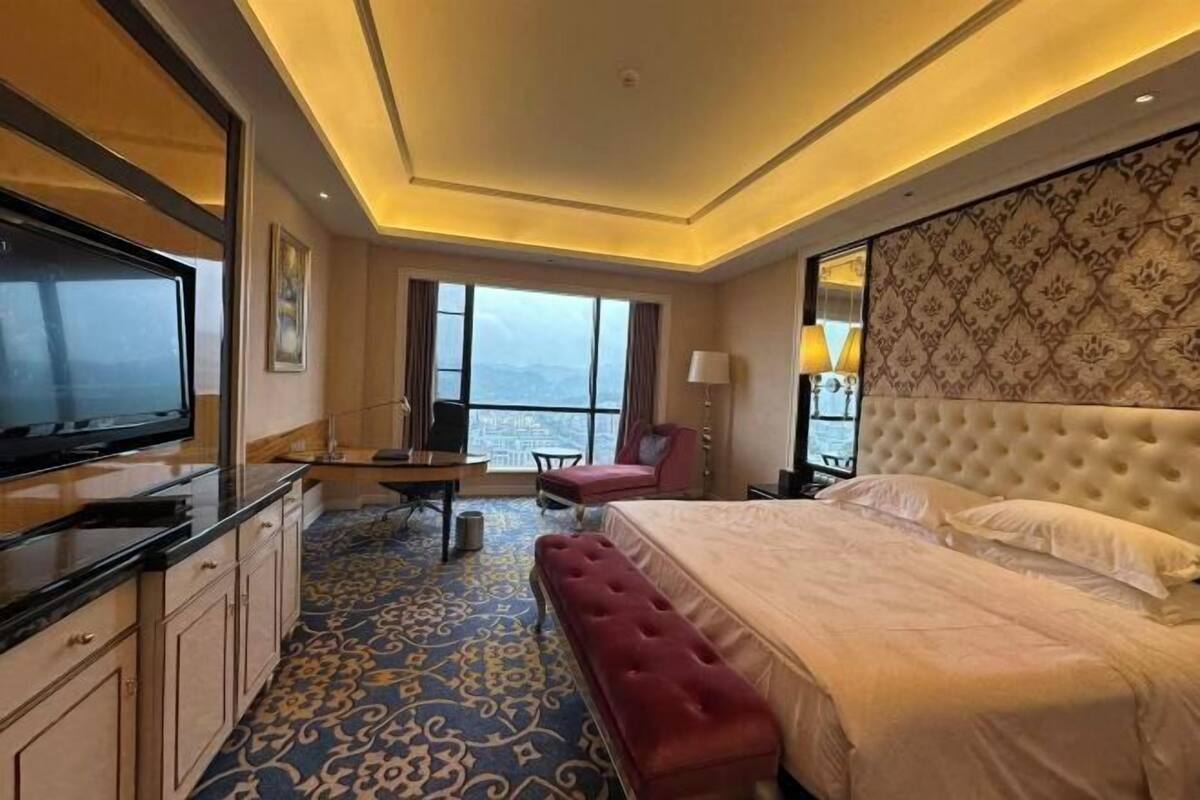 A hotel room with a large bed, a TV, a desk, and a view of the city.