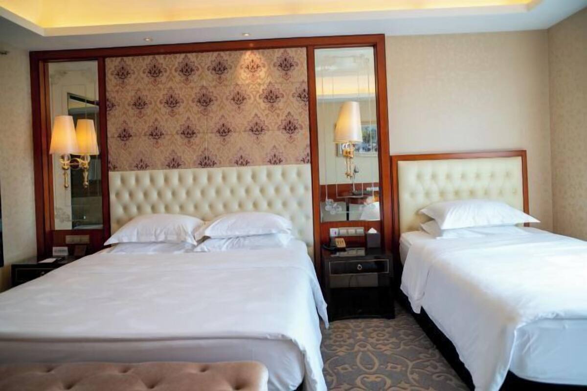 A hotel room with two beds, a large mirror, and a patterned wallpaper.