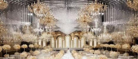 Un salón amplio con un pasillo central, candelabros ornamentados y arreglos florales.