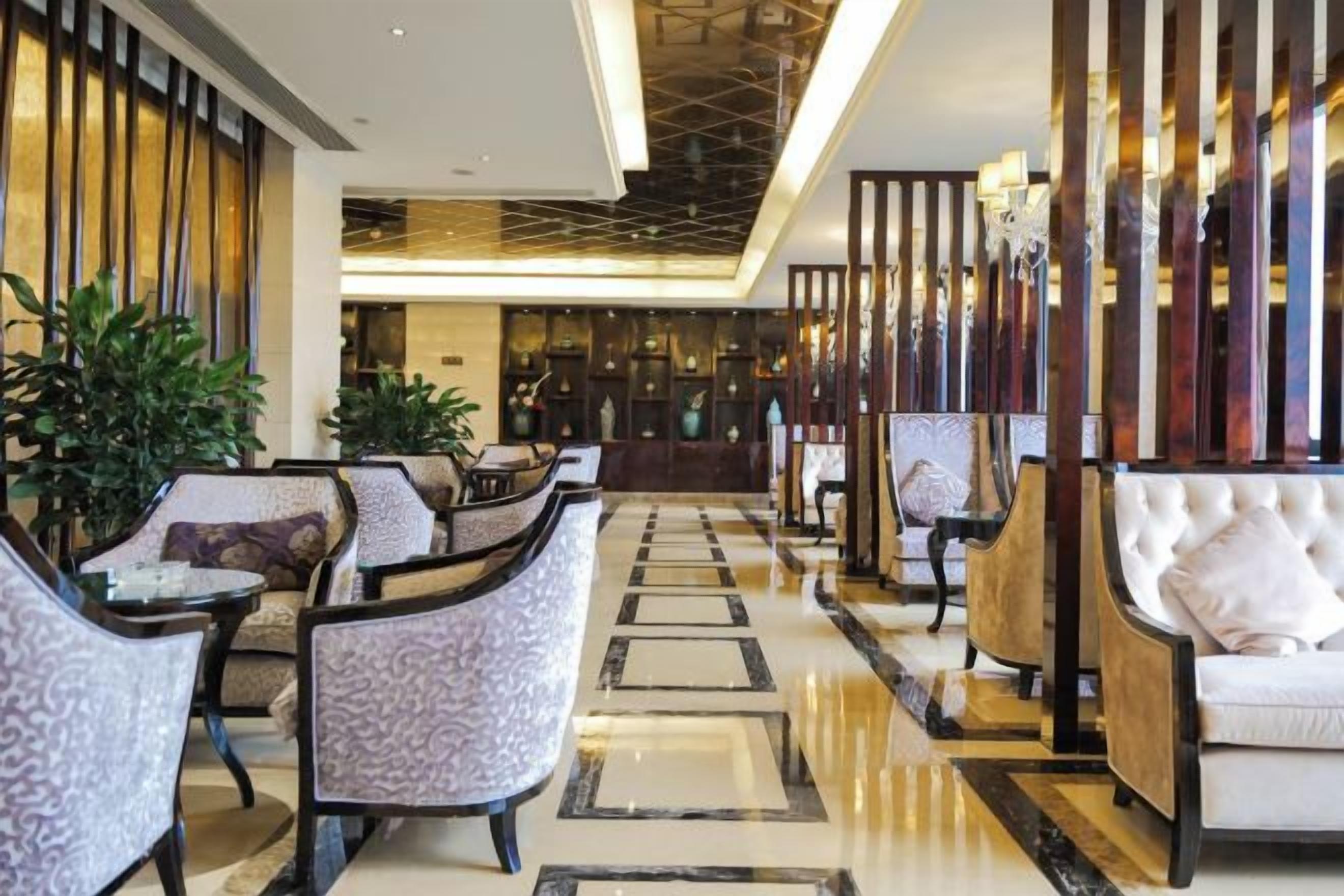 Un vestíbulo de hotel con un mostrador de recepción alargado, un área de descanso con sillas y sofás, y una pared decorativa con elementos verticales.
