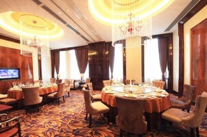 Comedor de hotel con mesas redondas, sillas, candelabros y una pantalla de televisión.