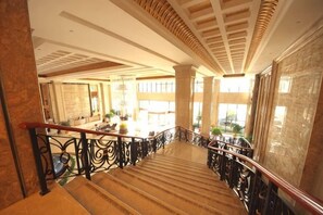 A grand staircase with ornate railings, leading to a well-lit area with large windows and a view of the outdoors. - Jasmine International Hotel (Renshou)