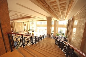 Una amplia escalera con barandillas ornamentales, que conduce a un espacio bien iluminado con ventanas grandes y vistas al exterior.