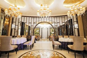Uma sala de jantar formal com mesas, cadeiras, lustres e um arco central.