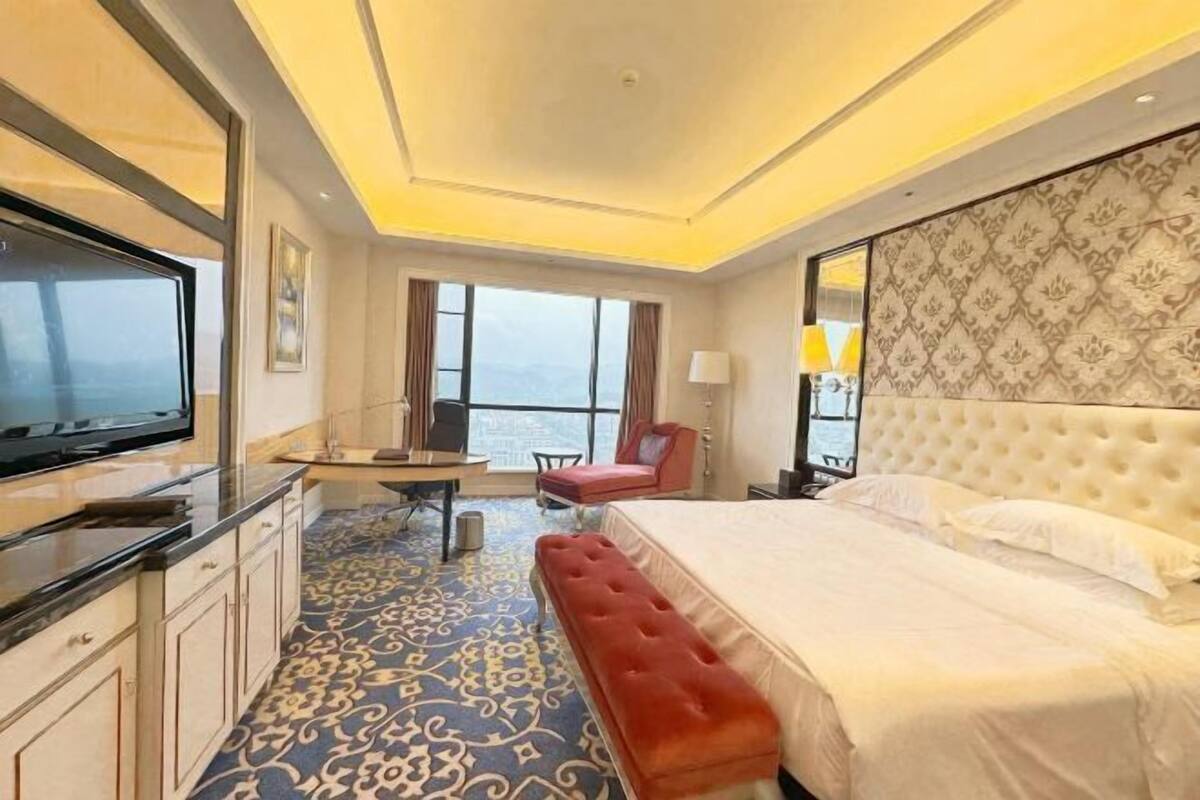 A hotel room with a large bed, a TV, a desk with a chair, and a view of the sea.