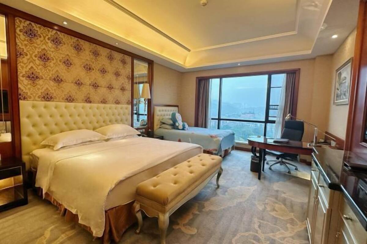 A hotel room with a large bed, a desk, a chair, and a view of the city.