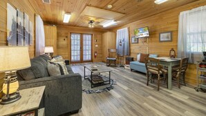 L’intérieur d’un chalet accueillant, avec un plafond en bois, un canapé, une table à manger avec des chaises et un téléviseur.