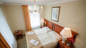 Habitación de hotel con cama, mesita de noche, lámpara, un cuadro en la pared y ventana con cortinas.