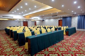 A conference room with rows of tables, yellow chairs, and a red carpeted floor.