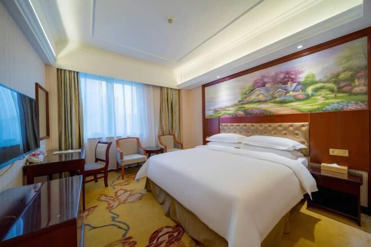 Une chambre d’hôtel avec un grand lit, un bureau avec une chaise, une télévision et un tableau au mur.