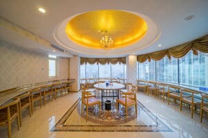 Un comedor de hotel con una mesa redonda rodeada de sillas, una araña y ventanas amplias.