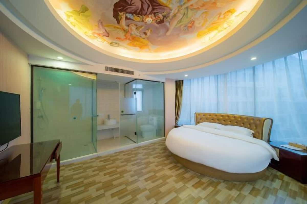 Une chambre d’hôtel dotée d’un grand lit, d’une douche en verre, d’une télévision et d’une fresque peinte au plafond.