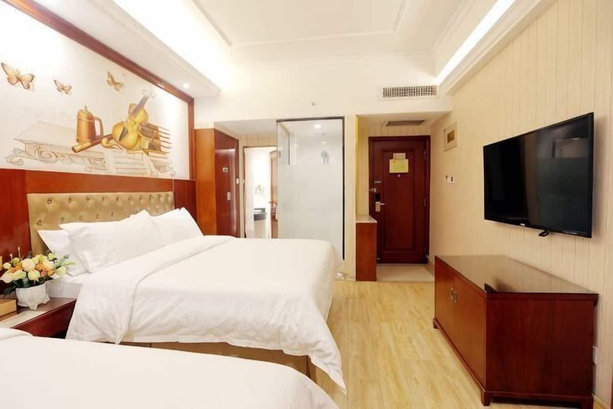 Une chambre d’hôtel avec deux lits, une télévision, une commode en bois et un tableau au mur.