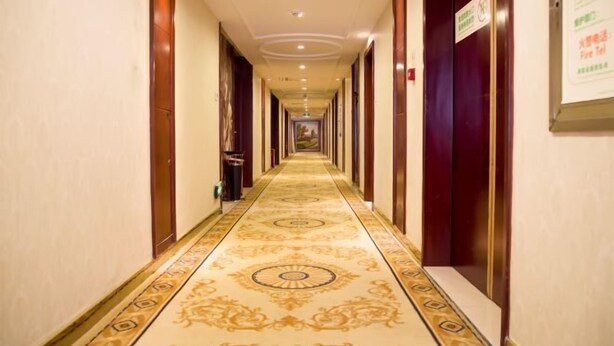 A hotel hallway with a patterned carpet, wooden doors, and a sign indicating a fire exit. - Vienna Hotel (Jishou Railway Station) (Jishou)