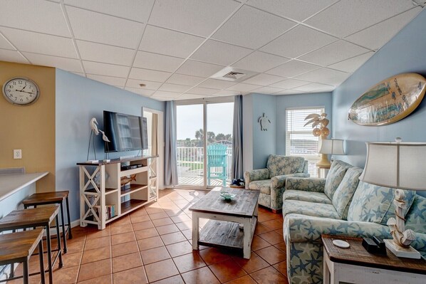 A living room with a TV, sofa, coffee table, and a balcony with chairs.