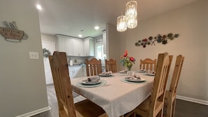 A dining area with a table set for six, wooden chairs, a vase with flowers, and pendant lights.