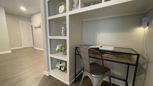 A room with a glass desk, a metal chair, and white shelving with decorative items.