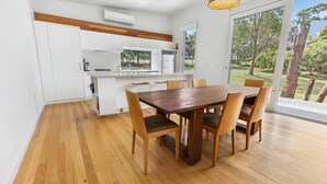 Eine moderne Küche mit weißen Schränken, einem Holzespeisetisch mit sechs Stühlen und einem großen Fenster mit Blick ins Freie.