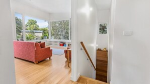 Ein modernes Interieur mit einer Holztreppe, einem roten Sofa und einem Blick ins Freie durch große Fenster.