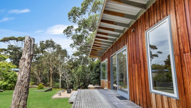 Eine moderne Holzterrasse mit großen Schiebeglastüren, die zu einem überdachten Außenbereich führen.
