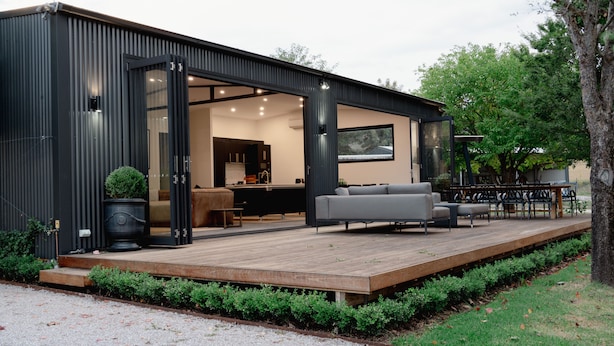 A modern, open-plan living space with a wooden deck, a grey sofa, and a dining area.