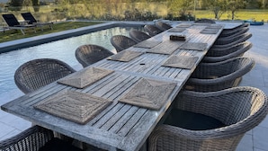 A long wooden table with woven placemats and wicker chairs around a pool.