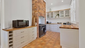 A kitchen with white cabinets, a brick wall, a microwave, a stove, and a tiled floor.